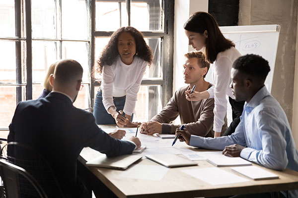 Rear view of a woman explaining new strategies to coworkers during conference meeting in office. Businesspeople meeting in office board room for new project discussion.