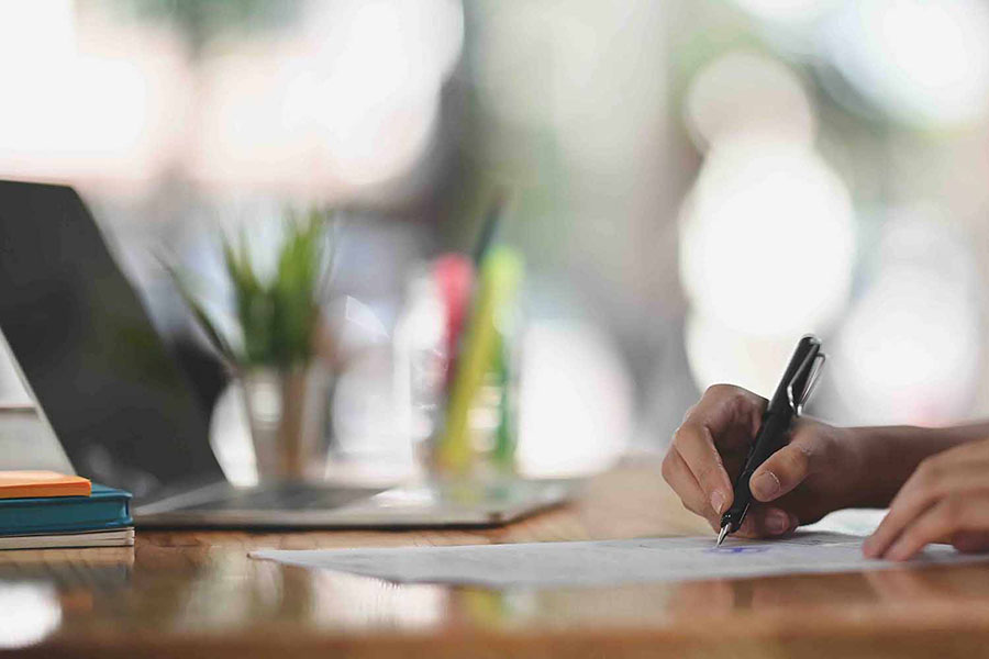 Laptop computer and person holding a pen and reviewing a paper document