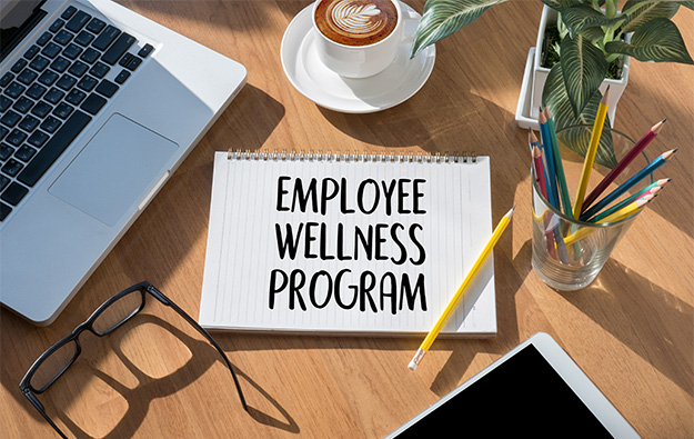 Lapotop, coffee, glasses, pad with writing 'Employee Wellness Program'